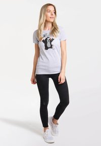 Gray cotton t-shirt featuring a cartoon mole graphic. It has a classic fit, short sleeves, and is paired with black skinny jeans and white sneakers.