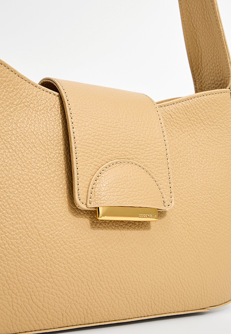 Beige Lederhandtasche mit strukturiertem Finish, ausgestattet mit einem Klappenverschluss und goldenen Hardware-Details. Minimalistisches Design mit weichen Kanten.