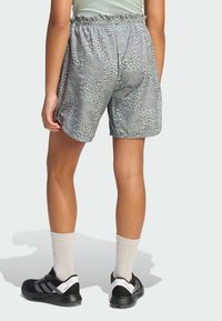 Szorty w panterkę z elastycznym pasem, wykonane z lekkiej tkaniny, w połączeniu z czarnymi butami sportowymi i kremowymi skarpetkami.