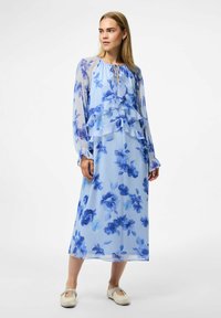 Prozračna plava cvjetna maksi haljina s naboranim slojevima, prozirnim rukavima i dekolteom s vezicom. Ima laganu, teksturiranu tkaninu.