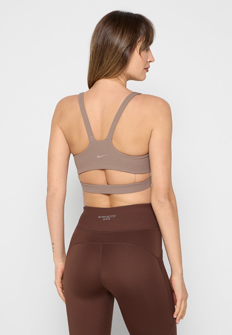 Brauner Sport-BH mit gerippter Textur, breiten Trägern und ausgeschnittenem Rücken. Kombiniert mit hoch taillierten, braunen Leggings mit einem Logo.