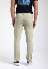 Pantaloni beige chiaro in cotone, slim fit, con due tasche posteriori e una texture pulita e liscia, abbinati a sneaker bianche.