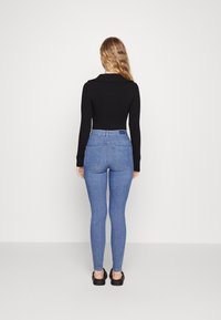 Fekete, hosszú ujjú felső, magas derekú világoskék, skinny farmernadrággal párosítva. Simaságot árasztó anyag, testhezálló fazon, és két hátsó zseb látható.