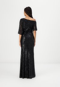 Abito nero di paillettes con design a spalle scoperte, maniche corte e una silhouette aderente che si allarga all'orlo.