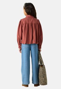 Chemise boutonnée en brun textured avec un dos froncé, associée à un jean taille haute bleu. Le mannequin porte un sac fourre-tout en imprimé léopard.