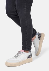 Baskets de sport blanches avec des lacets gris, un accent rose sur la languette et un talon à motif léopard. Semelle texturée avec une bonne adhérence.