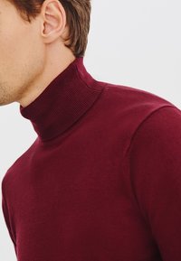 Burgundzki sweter z golfem, wykonany z miękkiego materiału, z prążkowanym kołnierzem i gładką fakturą, o dopasowanej sylwetce.