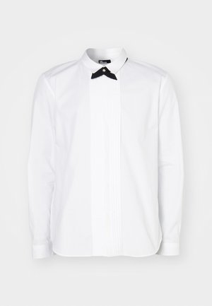 White long-sleeve shirt with a black bow tie, featuring a front placket with vertical pintuck details for texture and visual interest.