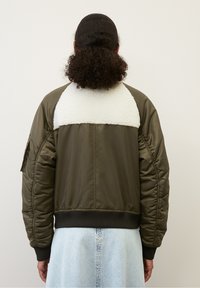 Olivengroene bomberjas met een witte fleece schouderstuk, geribbelde zoom en gestructureerde mouwen. Voorzien van zijzakken en gewatteerde details.