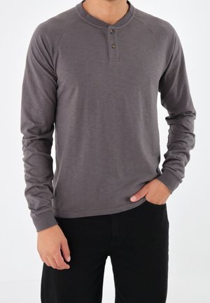 Graues Langarm-Henley-Shirt mit rundem Ausschnitt, dreiknöpfiger Knopfleiste und Raglanärmeln. Hergestellt aus einem weichen, strukturierten Stoff.