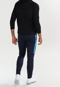 Męska odzież sportowa składająca się z czarnej bluzki z długim rękawem oraz granatowych spodni z niebieskim paskiem po bokach. Wykonana z gładkiego, elastycznego materiału.