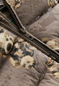 Primo piano di un giubbotto imbottito marrone bagnato con stampa di orsetti e un tirazip a forma di stella.