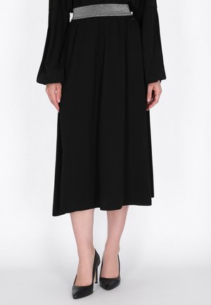 Modelo con una falda negra hasta media pantorrilla, una cintura ancha plateada y zapatos negros de tacón con punta.