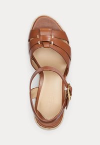 Sandal in pelle marrone con cinturini incrociati, fibbia alla caviglia regolabile e suola in espadrilles intrecciata. Texture liscia, design a punta aperta.