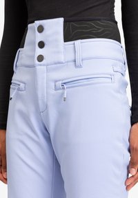 Lichtblauwe broek heeft een hoge taille met drie zwarte knopen en twee ritszakken aan de voorkant. De stof lijkt glad en aansluitend.