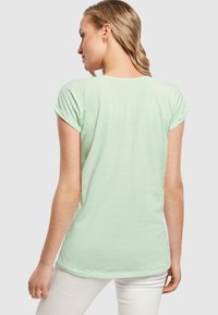 Vaalean mintunvihreä t-paita, jossa on kierretyt lyhyet hihat, pyöreä kaula-aukko ja rento malli. Valmistettu pehmeästä, kevyestä kankaasta, jossa on sileä pinta.