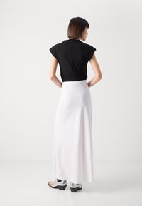 Black short-sleeve top with a back zipper, paired with a long white skirt. Footwear features silver accents and a block heel design.