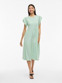 Mintgrön bomullsklänning med korta ärmar, en åtsittande liv och en tierad, medellång kjol. Bärs med svarta sandaler, slät textur.