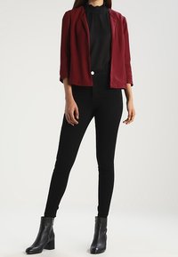 Burgundy fitted blazer over black high-neck blouse, paired with black skinny jeans and textured black ankle boots.