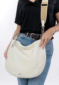 Borsa hobo in pelle bianca con finitura texturizzata, hardware in argento e una tracolla regolabile beige. La forma liscia e curva esalta il suo design.