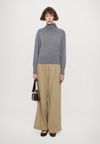 Grå turtleneck genser, løse beige vide bukser, brune slip-on sko og en liten mørk håndveske. Minimalistisk design, myke teksturer.