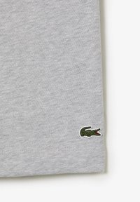 Gray cotton T-shirt featuring a small green crocodile logo stitched on the lower hem. Simple design with soft texture and short sleeves.