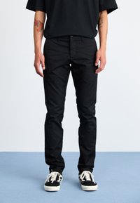 Fekete pamut nadrág slim fit szabásban, elől gombos záródással és öt zsebbel, fekete-fehér sportcipőkkel párosítva.