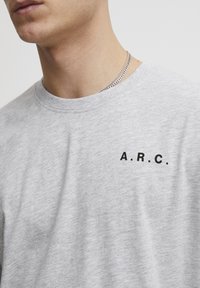 Grå bomull t-skjorte med rund hals og korte ermer, med en svart trykt logo "A.R.C." på venstre brystområde.
