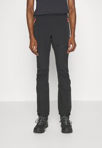 Svart utendør bukser laget av elastisk materiale, med glidelåslommer og orange detaljer, samt en slim fit design. Teksturert overflate.