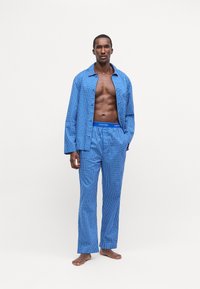 Set de pijama cu carouri albastre realizat dintr-un material moale, compus dintr-o cămașă cu nasturi, cu mâneci lungi, și pantaloni asortați, amândouă dotate cu un sistem de talie elastic.