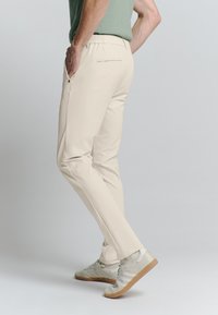 Beige broeken met een slim fit, elastische tailleband en zijzakken. Draagt met lichte sneakers, die een gladde stofstructuur laten zien.