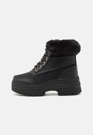 Bottes noires à la cheville avec un col en fausse fourrure, cuir texturé, côtés lisses, bout rond et semelle en caoutchouc épais avec motif cranté.