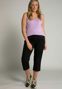 Lichtpaarse tanktop, zwarte cropped broek met ritszakken en zwarte sneakers met beige details; gladde stof en casual pasvorm.