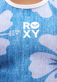 Tissu à motif floral bleu avec le logo blanc "ROXY" et un symbole de cœur stylisé près de la zone de la poitrine d'un vêtement sans manches.