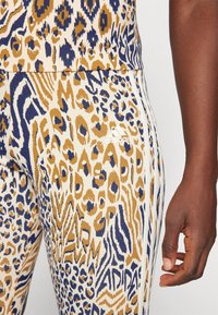 Djurmönstrade leggings med färgerna beige, marinblå och kräm; tillverkade av texturerat material med vita ränder och diskret varumärkning nära midjan.