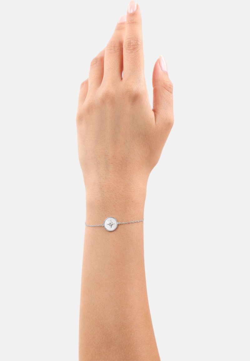 Bracciale in argento con un ciondolo rotondo dal design a forma di bussola. Il bracciale è delicato e riposa su una mano con un tono di pelle neutro.