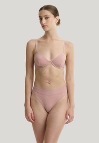 Soutien-gorge rose clair avec armatures, texture lisse, bretelles réglables, associé à un shorty taille haute assorti avec une ceinture tonale.