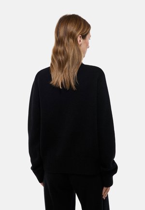 Pull noir en tricot avec une coupe ample, des poignets et un ourlet côtelés. Présente un col rond et est fabriqué en tissu texturé. Vu de dos.
