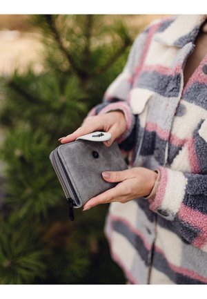 Gray leather wallet with a zip closure, featuring a black metal accent and a white pull tab, held in hands against a natural background.