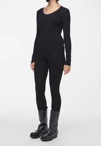 Black ribbed long-sleeve top with a scoop neckline, paired with black slim-fit pants and knee-high black boots with thick, textured soles.
