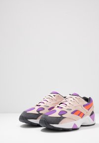 Sneakers med en ljusrosa ovandel, lila och orange detaljer, grå mocka på tån och vit sula. Har snörningsdesign och nätstruktur.