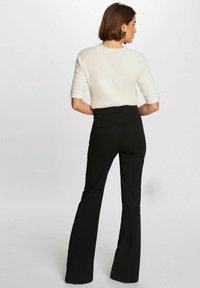 Maglione bianco a trama con maniche corte abbinato a pantaloni neri a vita alta a palazzo con tasche posteriori e una finitura liscia.