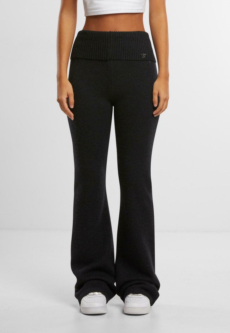 Black flared pants with a ribbed waistband and logo detail. Soft fabric texture, fitted at the hips with a relaxed fit through the legs.