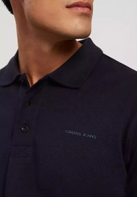 Granatowa koszulka polo wykonana z teksturowanej tkaniny, z trzema guzikami przy dekolcie i dyskretnym logiem "CROSS JEANS" na piersi.