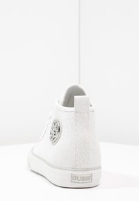 Biały wysoki tenisówka z płótnem, z teksturowaną powierzchnią, okrągłym akcentem z logo i solidną gumową podeszwą. Pętla z tyłu ułatwiająca zakładanie.