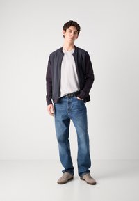 Ναυτική bomber jacket με σκούρο μανίκι, γκρι T-shirt, μπλε τζιν και μπεζ αθλητικά παπούτσια. Απλός σχεδιασμός, υφασμάτινη υφή και χαλαρή εφαρμογή.