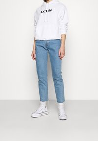 Felpa bianca con logo "Levi's", jeans boyfriend blu chiaro a gamba dritta e scarpe sportive bianche alte. Tessuto morbido, vestibilità casual e orlo sfrangiato.
