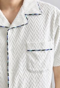 Valge tekstuuriga lühikeste varrukatega särk, millel on kalasabamuster. Krae ja tasku ääres must ja sinine ääristus. Kolme nööbiga kinnitus.