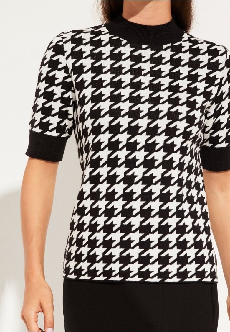 Femme portant un haut à manches courtes à motif pied-de-poule noir et blanc avec des poignets et un col côtelés noirs.