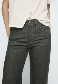 Donkergrijze denimjeans met gele stiksels, vijfzakontwerp en een metalen knoopsluiting. Tapered vorm met een gestructureerde afwerking.